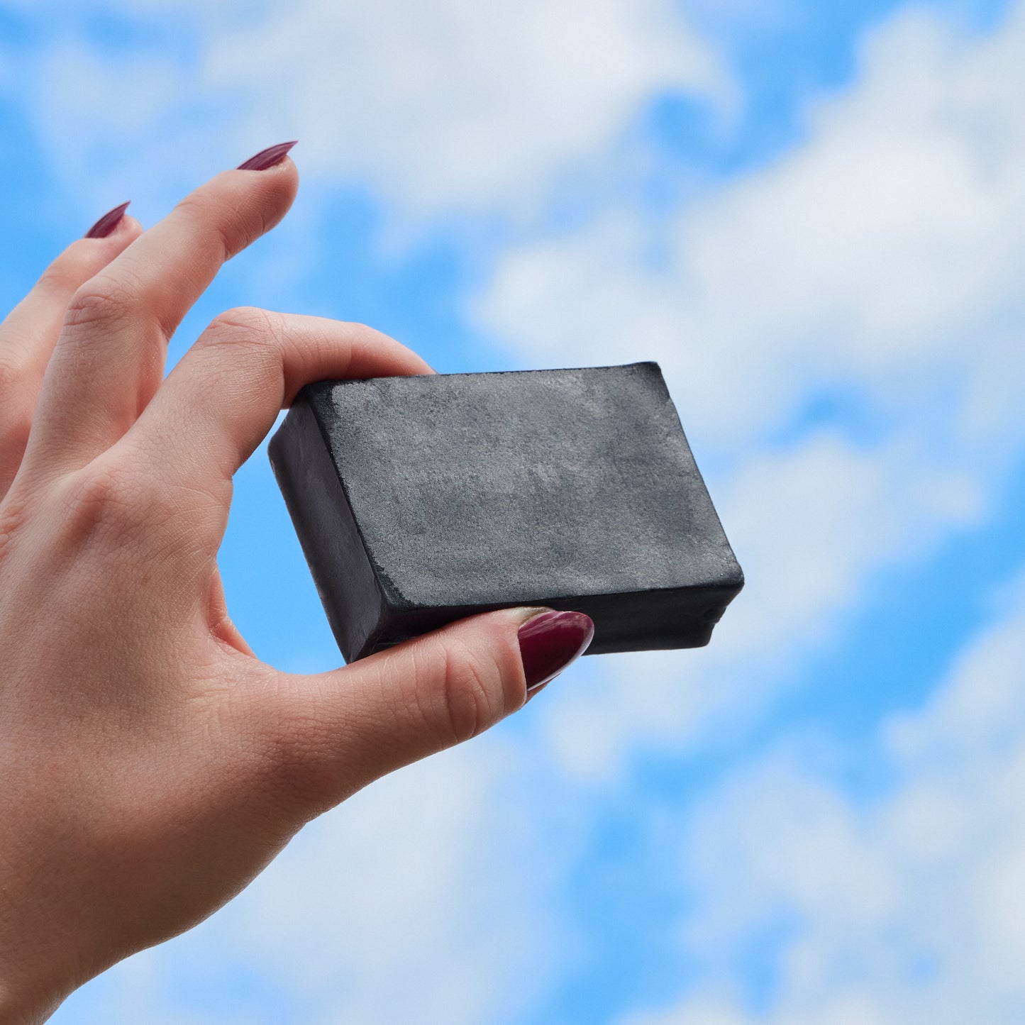 Hand holding a black soap bar against a blue sky background